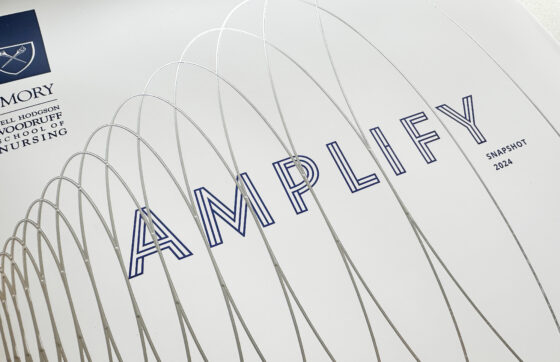 Closeup of "Amplify" cover with silver spiral in foil stamp raised above the print that says "Amplify: Snapshot 2024" and has the Emory School of Nursing logo